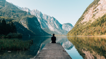 person sat at a lake between mountains